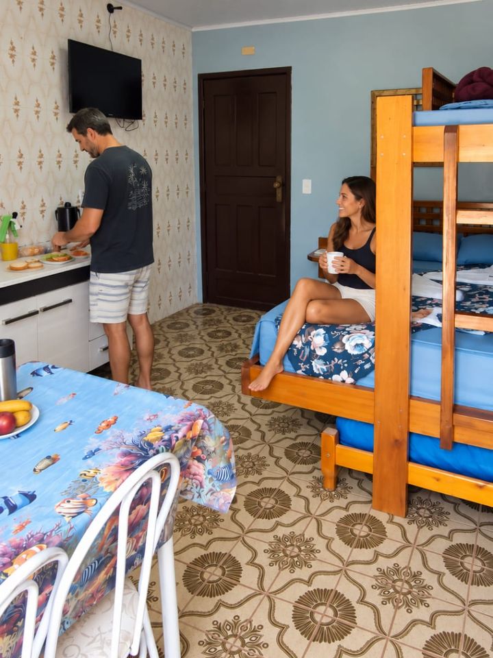 Casal hospedado na kitnet, com beliche e cozinha ao fundo