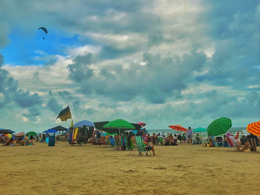 Praia movimentada em Torres com guarda-sóis e parapentes no céu